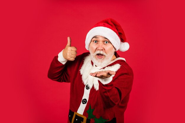 Czas świętować. radość z ferii zimowych. zabawny starszy mężczyzna w stroju świętego mikołaja. szczęśliwego nowego roku 2021. wesołych świąt. brodaty santa w kapeluszu na czerwonym tle. prezenty świąteczne i czas na zakupy upominkowe.