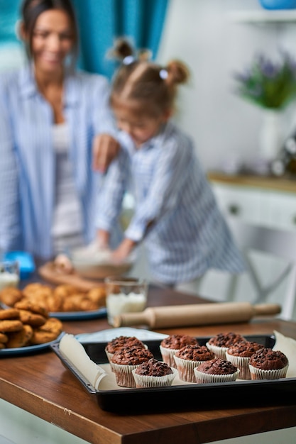 Czekoladowe babeczki na tacy w kuchni, w ścianie mama i córka pieką ciasteczka