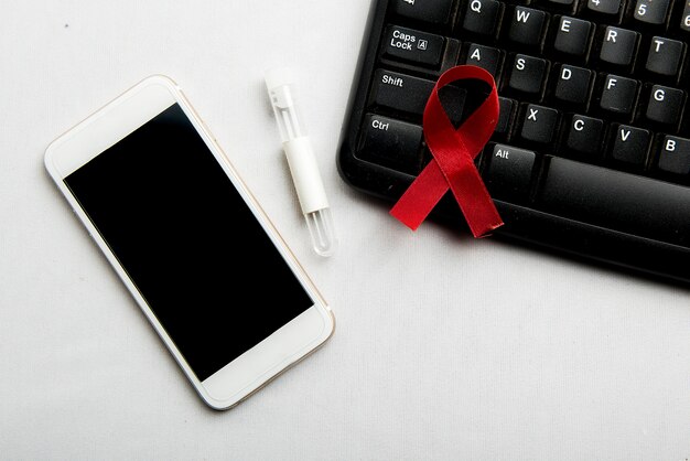 Czerwona wstążka i telefon komórkowy z białym tłem. Świadomość wstążki HIV Aids