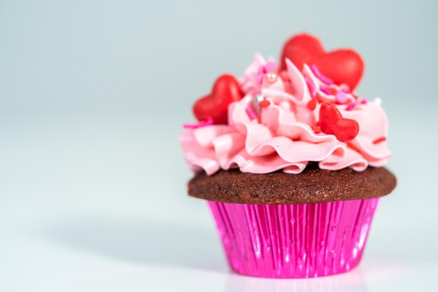 Czerwone aksamitne babeczki z różowym włoskim lukrem typu buttercream i ozdobione czerwonymi czekoladkami w kształcie serc i pocałunków.