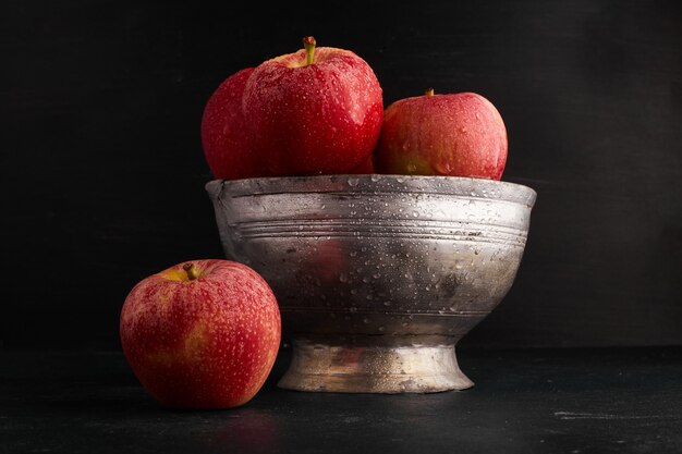 Bezpłatne zdjęcie czerwone jabłka w metalowej filiżance na czarnej powierzchni.