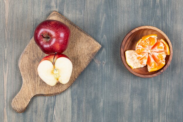 Bezpłatne zdjęcie czerwone jabłko na drewnianej desce z miską segmentów mandarynki