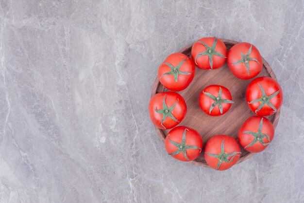 Bezpłatne zdjęcie czerwone pomidory w drewnianym talerzu na marmurze