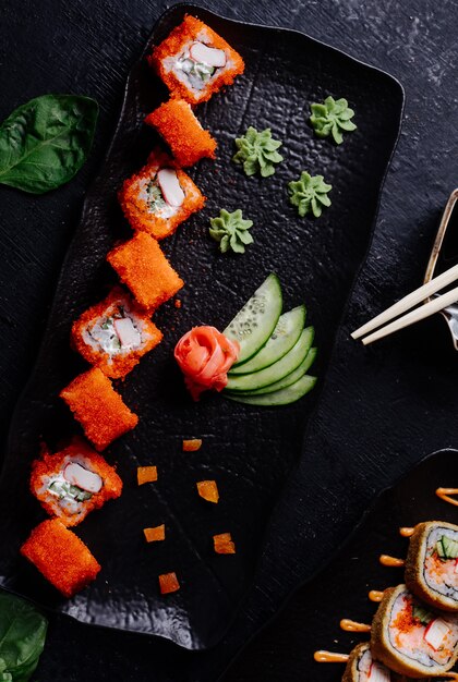 Czerwone rolki sushi z wasabi, imbirem i ogórkiem w czarnej płycie.