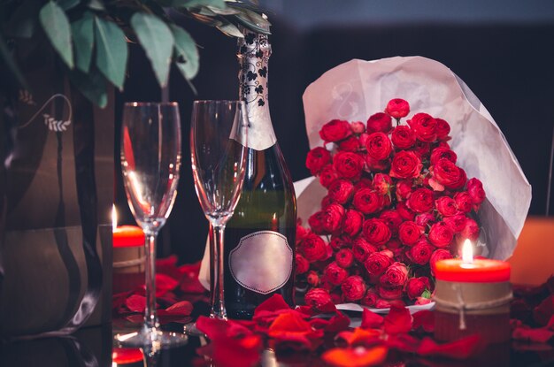 Czerwone róże, dwie szklanki, butelka szampana i świeca na stole