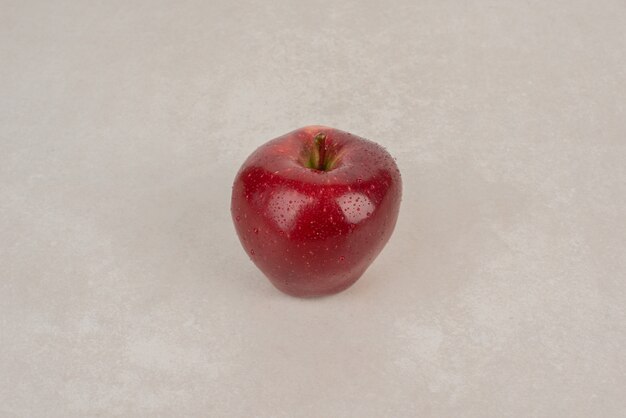 Czerwone, świeże jabłko na białym stole.