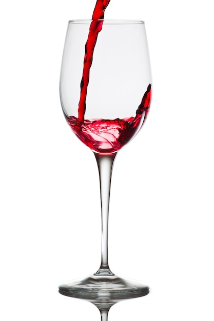Czerwone wino wlewa się do szklanki na białym tle na białej ścianie