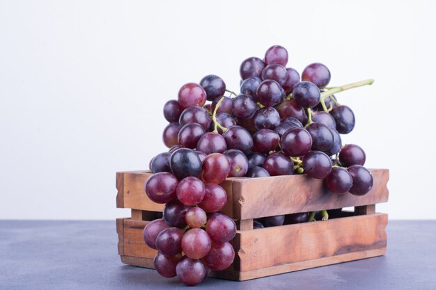Czerwone winogrona w drewnianej tacy na niebieskiej powierzchni