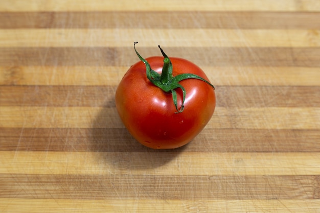 Czerwony pomidor z kroplami wody na drewnianej desce do krojenia