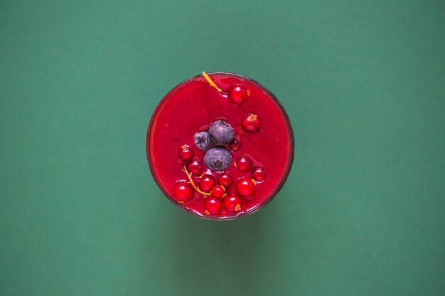 Czerwony smoothie z jagodami w szkle na zielonym tle