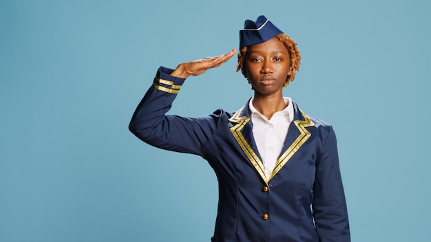 Bezpłatne zdjęcie członek załogi samolotu wykonujący salut wojskowy w studio, pokazujący krajowi wdzięczność przed kamerą. młoda stewardesa z zawodowym zawodem w mundurze lotniczym, wesoła i pewna siebie.