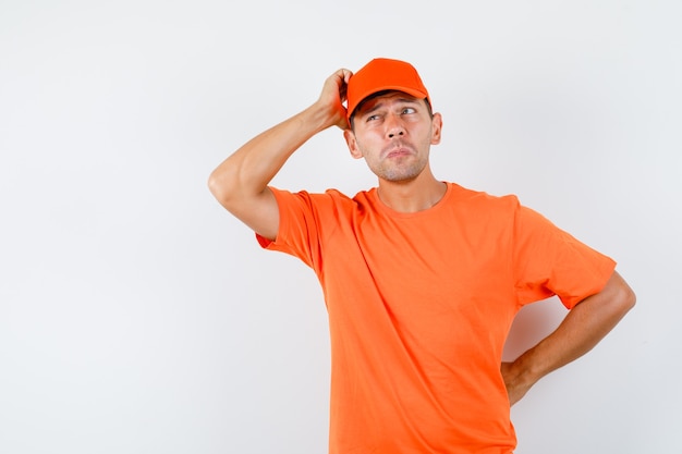 Bezpłatne zdjęcie człowiek dostawy drapie głowę w pomarańczowej koszulce i czapce i wygląda zamyślony