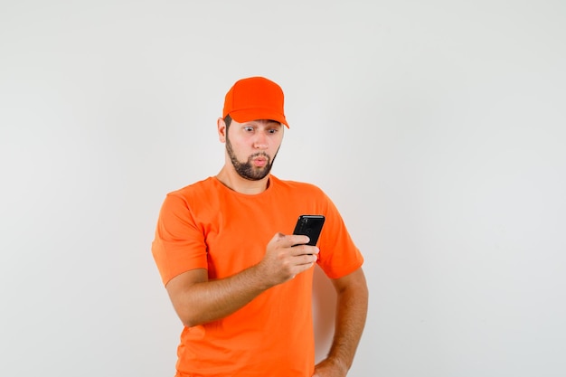 Człowiek dostawy patrząc na telefon komórkowy w koszulce, czapce i patrząc się zastanawiał. przedni widok.