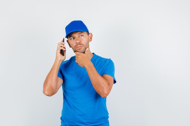 Człowiek dostawy, trzymając smartfon w pobliżu ucha w niebieskiej koszulce