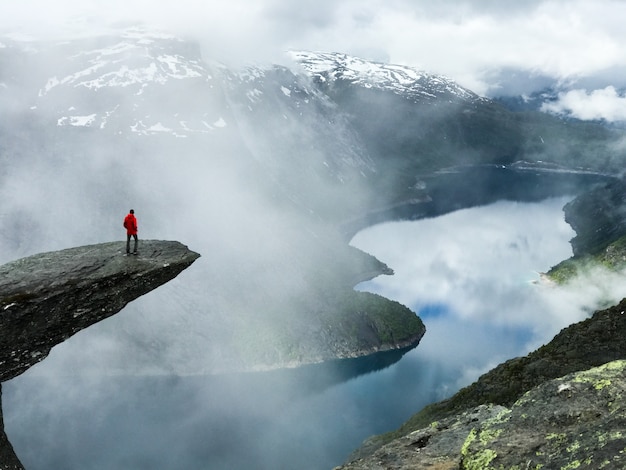 Człowiek siedzi pod koniec Trolltunga przed górami