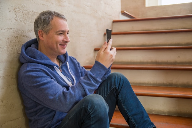 Człowiek SMS na telefon. Dorywcza miejskich przedsiębiorcy zawodowego przy użyciu smartphone uśmiecha się szczęśliwy wewnątrz budynku biurowego. Kryty portret nowoczesnego dojrzałego mę żczyznę z ruchomym na schodach