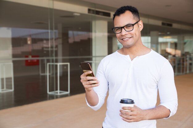 Człowiek SMS-y na telefon, trzymając na wynos kawy, patrząc na kamery