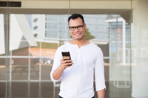 Człowiek stojący w budynku biurowym, trzymając w ręku telefon, uśmiechając się