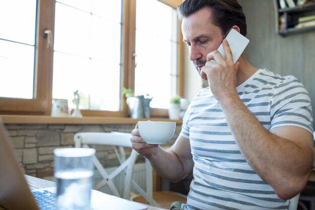 Człowiek trzyma filiżankę kawy i rozmawia przez telefon komórkowy