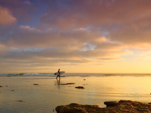 Człowiek z deską surfingową w morzu z pięknym zachodem słońca