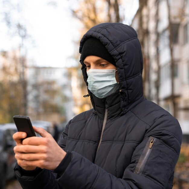 Człowiek z maską medyczną za pomocą smartfona na zewnątrz