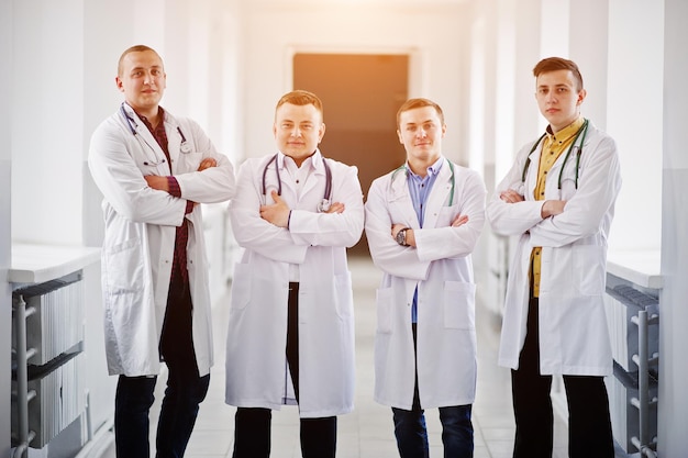 Czterech pewnych siebie lekarzy mężczyzn w białych fartuchach ze stetoskopami stojących na korytarzu w szpitalu