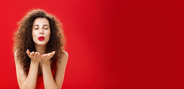 Bezpłatne zdjęcie czuła i delikatna stylowa kaukaska dziewczyna z kędzierzawą fryzurą i czerwoną szminką pochyloną w kierunku kamery