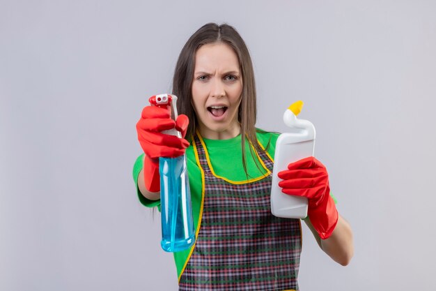 czyszczenie młoda kobieta ubrana w mundur w czerwonych rękawiczkach, trzymając środek czyszczący, trzymając spray do czyszczenia na odizolowanej białej ścianie