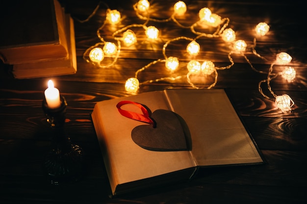 Czytanie książki na przytulny wieczór. świąteczny nastrój zdjęcie z bożonarodzeniowymi lampkami. drewniane serce i świeca. koncepcja hygge. idealny jesienny układ płaski.