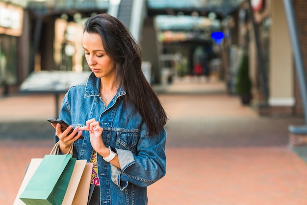 Dama z torba na zakupy używać smartphone w centrum handlowym
