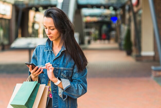 Dama z torba na zakupy używać smartphone w centrum handlowym