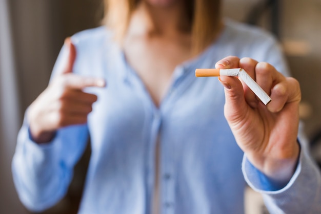 Defocus kobieta wskazuje przy łamanym papierosem