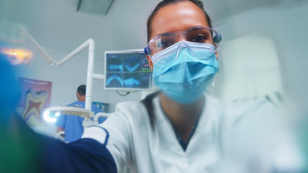 Dentysta pochylając się nad pacjentem zakładającym maskę tlenową przed zabiegiem w gabinecie stomatologicznym. lekarz pracujący w nowoczesnej klinice ortodontycznej w masce ochronnej i rękawiczkach podczas sprawdzania opieki zdrowotnej