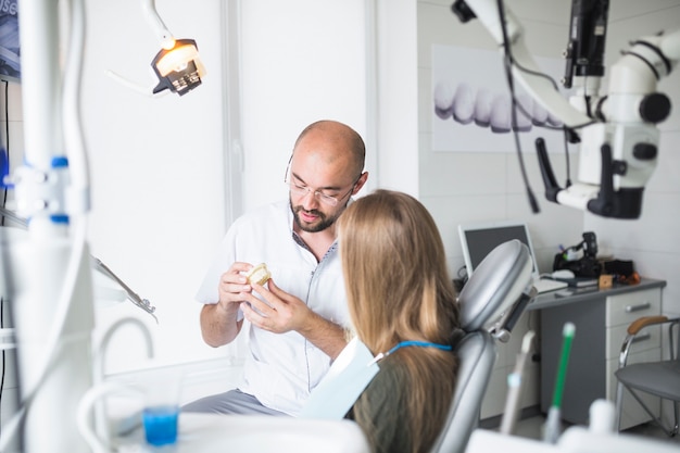 Dentysta pokazuje stomatologiczną szczękę jego żeńskiego pacjenta
