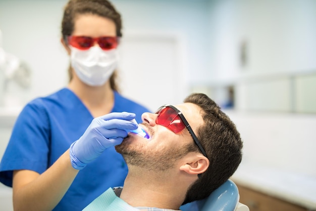 Dentysta sprawdzający średniego dorosłego mężczyznę światłem ultrafioletowym w klinice dentystycznej