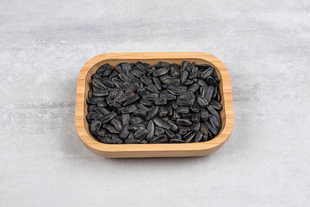 Deska pełna czarnych nasion słonecznika umieszczona na kamiennym stole.