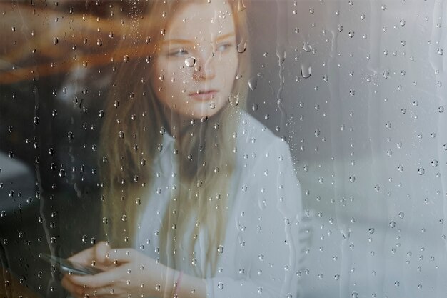 Deszczowe tło okna, kobieta używająca telefonu