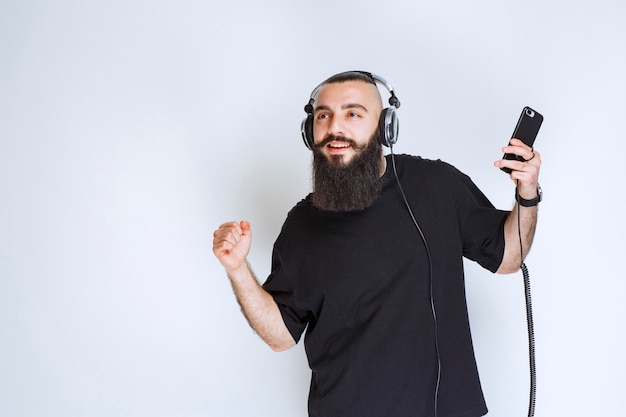 DJ z brodą w słuchawkach i słuchający playlisty na swoim telefonie.