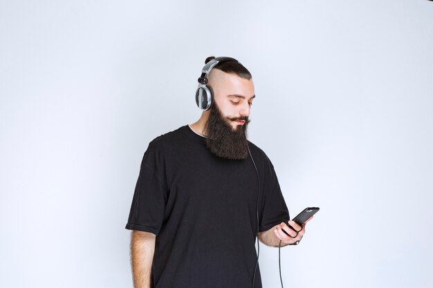 DJ z brodą w słuchawkach i ustawiający muzykę ze swojej playlisty na swoim smartfonie.