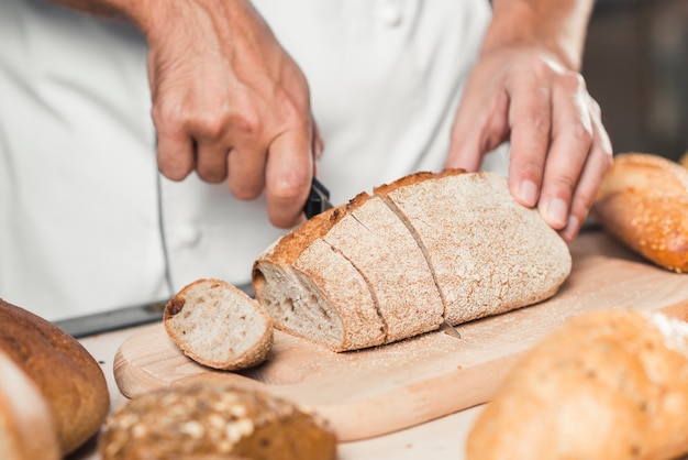 Dłoń Bakera wycinając świeży chleb nożem