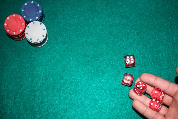 Dłoń gracza pokera rzucając czerwonymi kostkami na stole do pokera