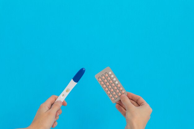 Dłoń trzymająca pigułki antykoncepcyjne i test ciążowy