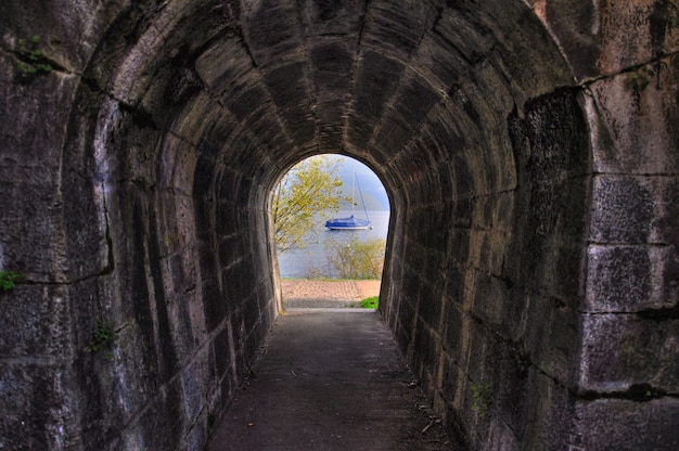Długie ujęcie łukowatego ceglanego tunelu z widokiem na jezioro z łodzią na przeciwległym końcu