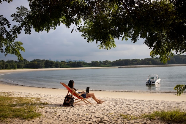 Długie zdjęcie kobiety pracującej na laptopie na plaży