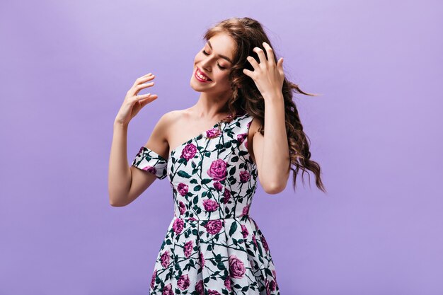 Długowłosy dama w pięknej sukni pozuje na fioletowym tle. Kędzierzawy radosna kobieta w stroje kwiatowe ładny uśmiech na na białym tle.
