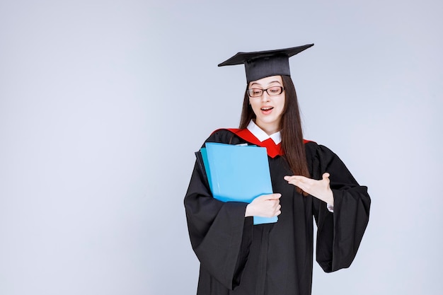 Długowłosy student w okularach pokazujący niebieskie foldery. Zdjęcie wysokiej jakości