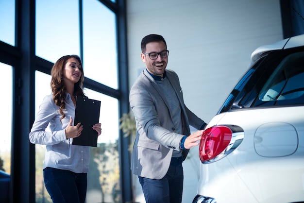 Dobrze ubrany biznesmen kupuje nowy samochód, a sprzedawca prezentuje klientowi nowy pojazd