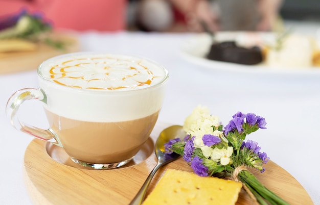 Dobrze udekorowany kubek gorącej kawy podawany na danie drewniane i mały fioletowy kwiat i herbatniki