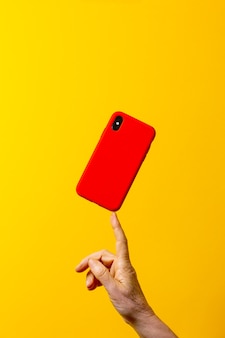 Dojrzała kobieta ręka trzyma czerwoną obudowę smartfona jednym palcem na żółtym tle