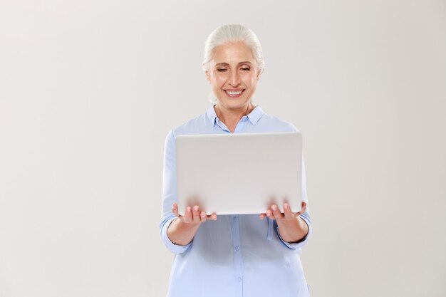 Dojrzała kobieta trzyma laptop odizolowywającego i używa